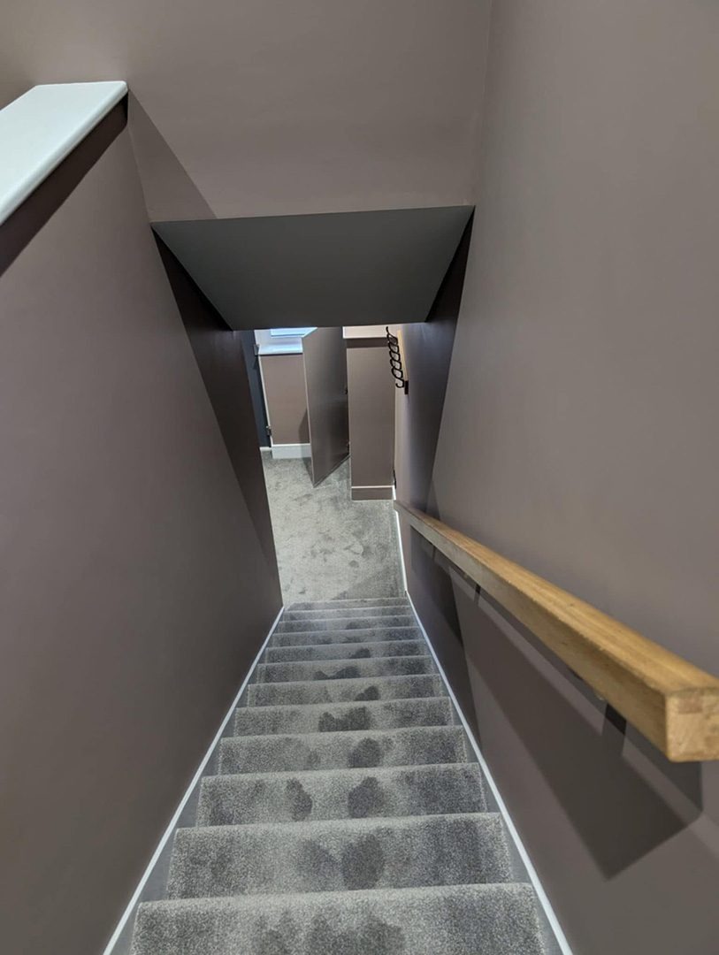Freshly painted staircase with grey carpet and timber handrail